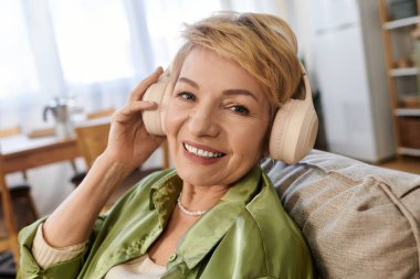 Kısa saçlı son sınıf öğrencisi kadın kanepede dinlenirken müzik dinliyor, mutluluk saçıyor..