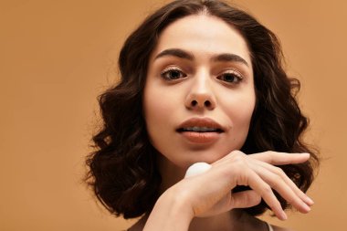 Bir stüdyo ortamında, genç bir kadın kendine güvenen bir gülümseme ile cilt rutinini paylaşır..