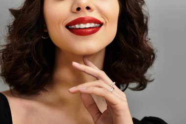 Neşeli genç bir kadın, diş tellerini ve kırmızı dudaklarını yumuşak, gri bir arka plana vuruyor..