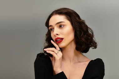 Göz kamaştırıcı genç bir kadın, diş telleri ve canlı kırmızı dudaklarıyla gri renge karşı poz veriyor..