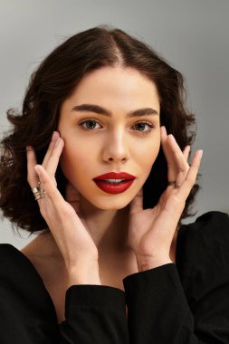 Göz kamaştırıcı kırmızı dudaklı bir kadın zarif bir şekilde gri bir zemine poz veriyor..