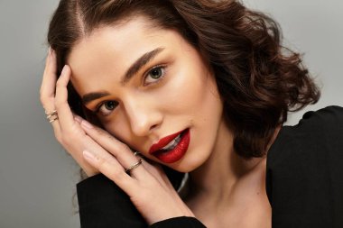 Diş teli takan genç bir kadın, canlı kırmızı dudaklarını sergileyerek gri bir zemine nazikçe poz veriyor..