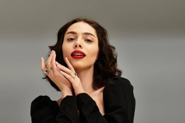 Kendine güvenen genç bir kadın zarif bir şekilde poz verir, kırmızı dudaklar ve parlak diş telleriyle tarzını sergiler..