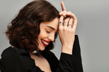 Genç bir kadın neşeyle ışıldar, diş tellerini ve kırmızı dudaklarını göstererek zarif bir şekilde ayakta durur..