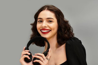 Çarpıcı kırmızı dudakları olan güzel bir genç kadın kulaklık tutarken ışıl ışıl gülümser..