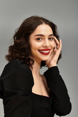 Genç bir kadın kendine olan güvenini parlak bir gülümseme ile gösteriyor, diş tellerini ve kırmızı dudaklarını vurguluyor..