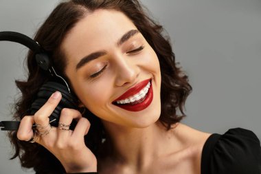 Parlak kırmızı dudaklar, müzik dinlerken neşesini vurgular, gençlik dolu bir güzellik saçar..