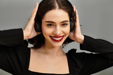 Kırmızı dudakları ve diş telleri olan neşeli genç bir kadın parlak bir şekilde gülümserken müzik dinler..