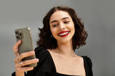 Kırmızı dudakları ve diş telleriyle gülümseyen genç kadın telefonuna bakıyor, neşe ve güven saçıyor..