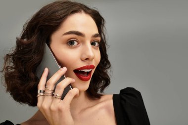 Güzel, genç bir kadın, gri bir arka planda diş telleri ve canlı kırmızı dudaklarıyla güvenle gülümsüyor..