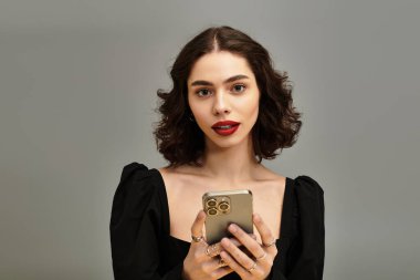 Güzel genç bir kadın elinde akıllı bir telefonla çarpıcı kırmızı dudaklarını sergiliyor..