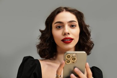 Kıvırcık saçlı, kırmızı dudaklı, akıllı telefonuyla meşgul olan çekici bir genç kadın..