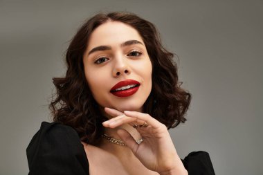 Çekici genç bir kadın zarif poz veriyor, parlak diş telleri ve parlak kırmızı dudaklarıyla gülümsüyor..