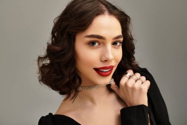 Canlı kırmızı dudakları olan genç bir kadın gri bir zemine karşı güven yayıyor..