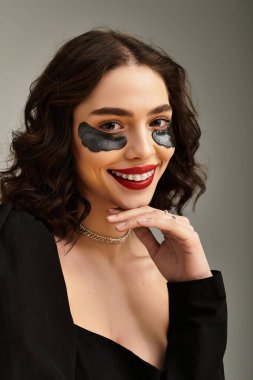 Çekici genç bir kadın kırmızı dudaklarını ve diş tellerini gösterirken aynı zamanda gülümsüyor ve kendinden emin poz veriyor..