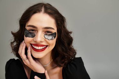 Tel ve kırmızı dudakları olan neşeli genç bir kadın yumuşak gri bir arka planda parıldıyor..