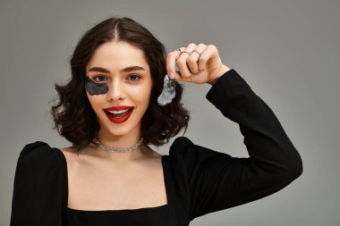 Göz kamaştırıcı kırmızı dudaklı genç bir kadın cilt bakımı yapar, ürünleri kendine güvenle tutar..