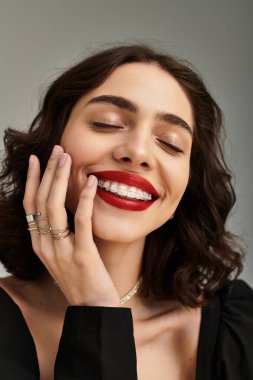 Diş teli takan genç bir kadın kendinden emin bir şekilde gülümsüyor, parlak kırmızı dudaklar ve neşeli bir ifade sergiliyor..