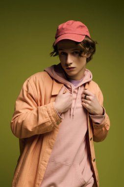 Moda kıyafetleri içinde genç bir adam parlak yeşil bir arka plana karşı güvenle poz veriyor..