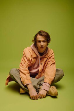 Şık bir genç adam, canlı yeşil bir zemin karşısında çağdaş bir şekilde cazibe yayar..