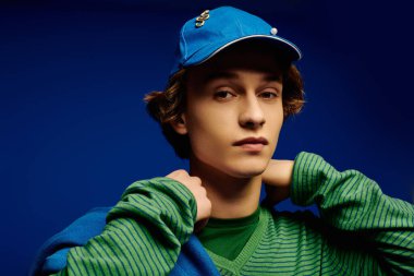 Genç bir adam, modaya uygun kıyafetini çarpıcı bir mavi zemine karşı özgüvenle ön plana çıkarıyor..