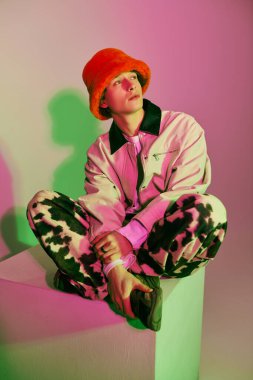 Genç bir adam bacak bacak üstüne atmış bir vaziyette oturuyor. Seçkin modern gençlik modasına uygun giyinmiş..