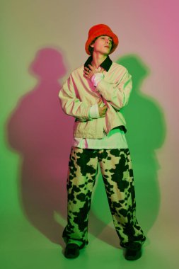 Moda kıyafetleri içinde genç bir adam, renkli ışıkların ortasında modern tarzda ışıl ışıl poz veriyor..