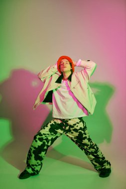 Genç bir adam renkli ışıklandırma efektleriyle çevriliyken kendine güvenle modaya uygun giysiler sergiliyor.