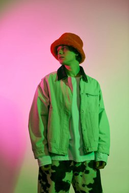 Şık bir genç adam canlı bir arkaplana karşı güven içinde poz veriyor, modern gençlik kültürünü somutlaştırıyor..