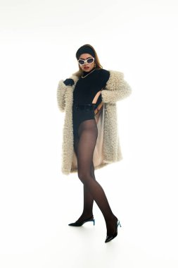 Şık, genç bir kadın şık kıyafetini ve güneş gözlüklerini parlak bir ortamda sergiliyor..