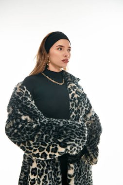 Leopar desenli bir ceket ve zarif aksesuarlar giyen genç bir kadın moda anlayışını sergiliyor..