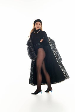 Genç bir kadın moda anlayışını canlı bir özgüvenle sergiliyor ve içeride poz veriyor..