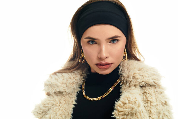 A beautiful young woman poses elegantly in a chic outfit against a bright background.