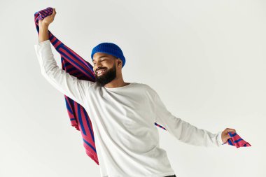 Şık bir genç adam neşeyle parıldıyor, neşe içinde parlak bir atkı tutuyor..