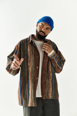 Genç bir adam minimalist bir stüdyoda kendine güvenerek poz veriyor, renkli kıyafetlerini sergiliyor..