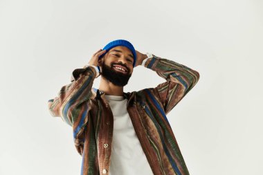 Sakallı yakışıklı adam ışıl ışıl gülümsüyor, moda anlayışını canlı bir ortamda sergiliyor..