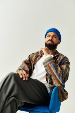Şık bir kıyafeti olan genç adam otururken düşünceli bir şekilde poz veriyor, modern tarzı sergiliyor..