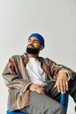 Yakışıklı genç adam modern bir mekanda rahatlıyor, canlı katmanlı bir kıyafeti kolaylıkla gösteriyor..