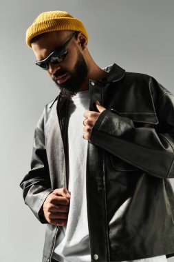 Yakışıklı bir adam deri ceket ve sarı bir bere giyer. Havalı bir tarzı ve kendine güveni vardır..