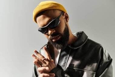 Şık bir adam modaya uygun kıyafetler giyerek minimalist bir stüdyoda rahatça poz verir..