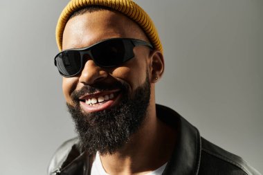 Güneş gözlüğü ve bere takan yakışıklı genç bir adam stüdyoda modaya uygun bir hava sergiliyor..