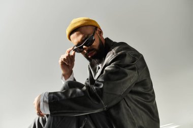 Güneş gözlüklü ve sarı bereli şık genç bir adam şehir ortamında rahatça poz veriyor..