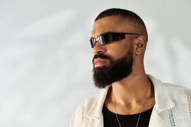 Genç adamın şık görünüşü, basit bir arkaplan karşısında modern kıyafetlerle parlıyor..