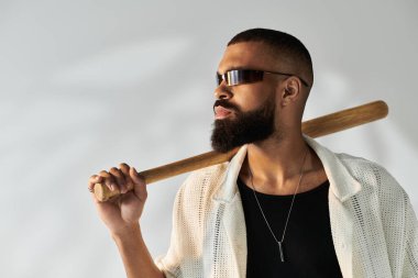 Sakallı, güneş gözlüklü, kendine güvenen bir adam. Sopayla şık bir arkaplanda poz veriyor..