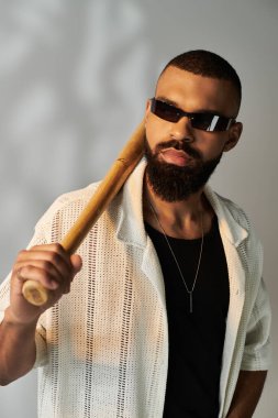 Sakallı ve güneş gözlüklü yakışıklı genç adam şık bir ortamda tahta bir yarasayla poz veriyor..