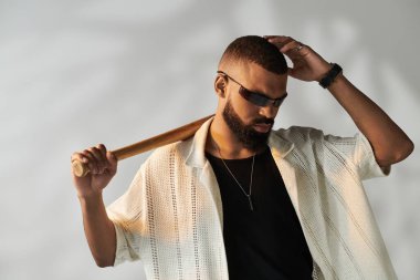 Genç bir adam modaya uygun bir ortamda beyzbol sopası tutarken kendine güvenerek tarzını sergiliyor..