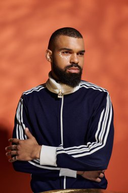 Yakışıklı şahıs, dikkat çekici turuncu arkaplan ve kentsel modayı somutlaştıran kendine güvenle poz veriyor..