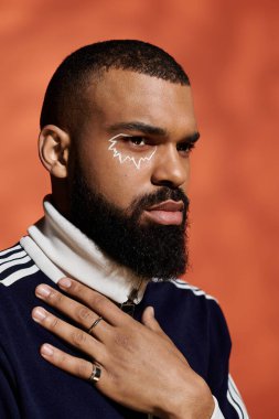 Yakışıklı genç adam kendine güveni tam, sportif kıyafetleri ve çarpıcı yüz sanatıyla poz veriyor..