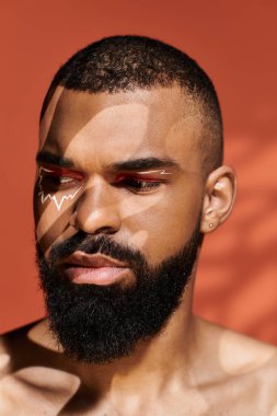 Genç adam hafif ışıklandırma altında çarpıcı bir yüz sanatı sergiliyor, kendine güveni ve tarzı var..