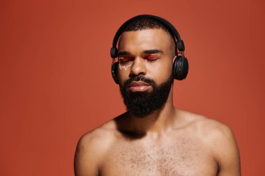 Sakallı genç adam kulaklık takarken müziği kucaklıyor, sanatsal ifadeler sergiliyor..